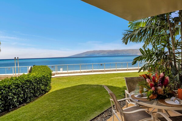 Une terrasse avec une table et des chaises, un arrangement floral et une vue sur l’océan.