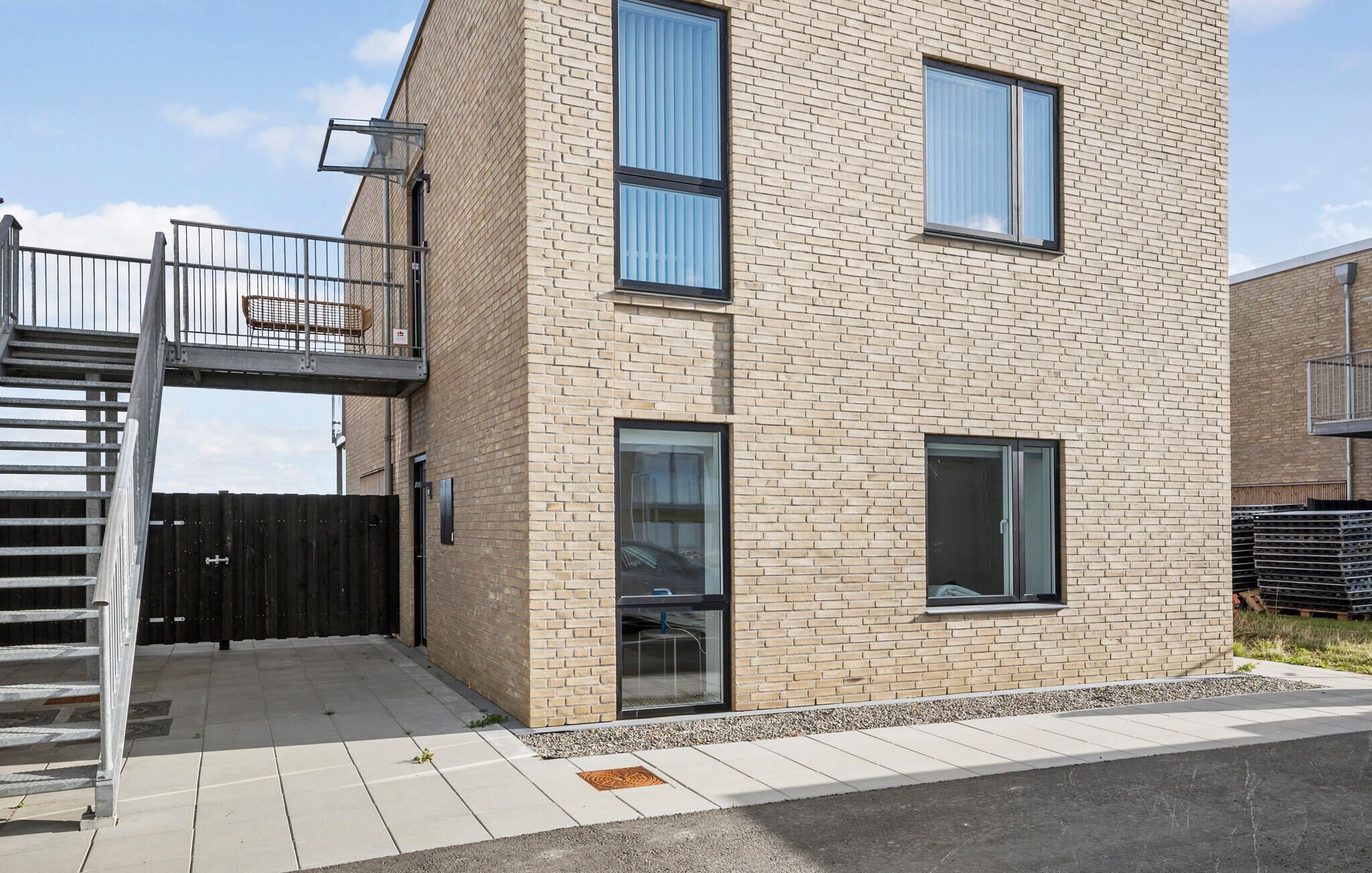 A modern two-story building with a brick facade, large windows, and a metal staircase leading to a balcony.