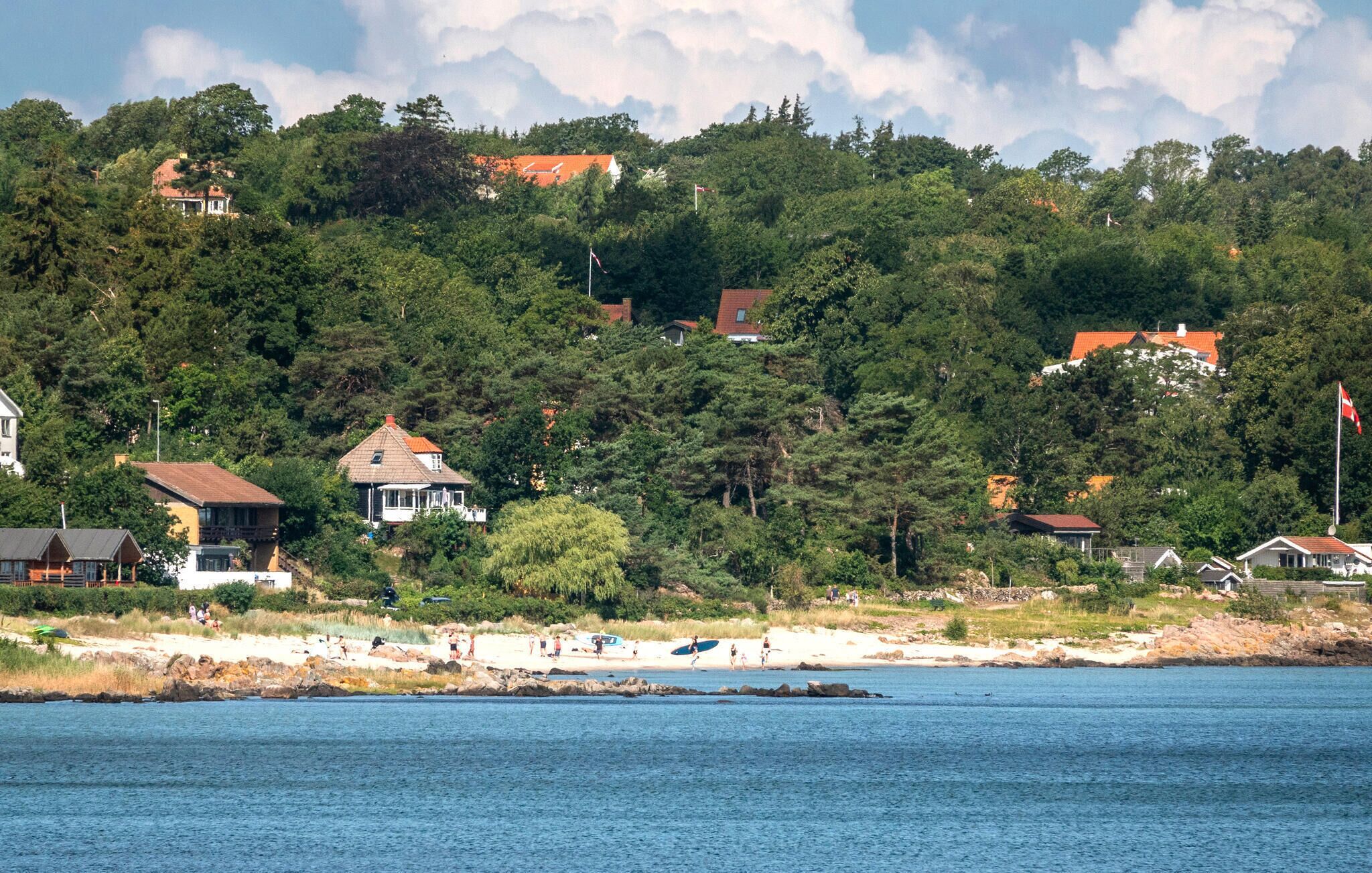 Ett kustområde med hus som ligger på en sluttning, en strand och ett lugnt hav.
