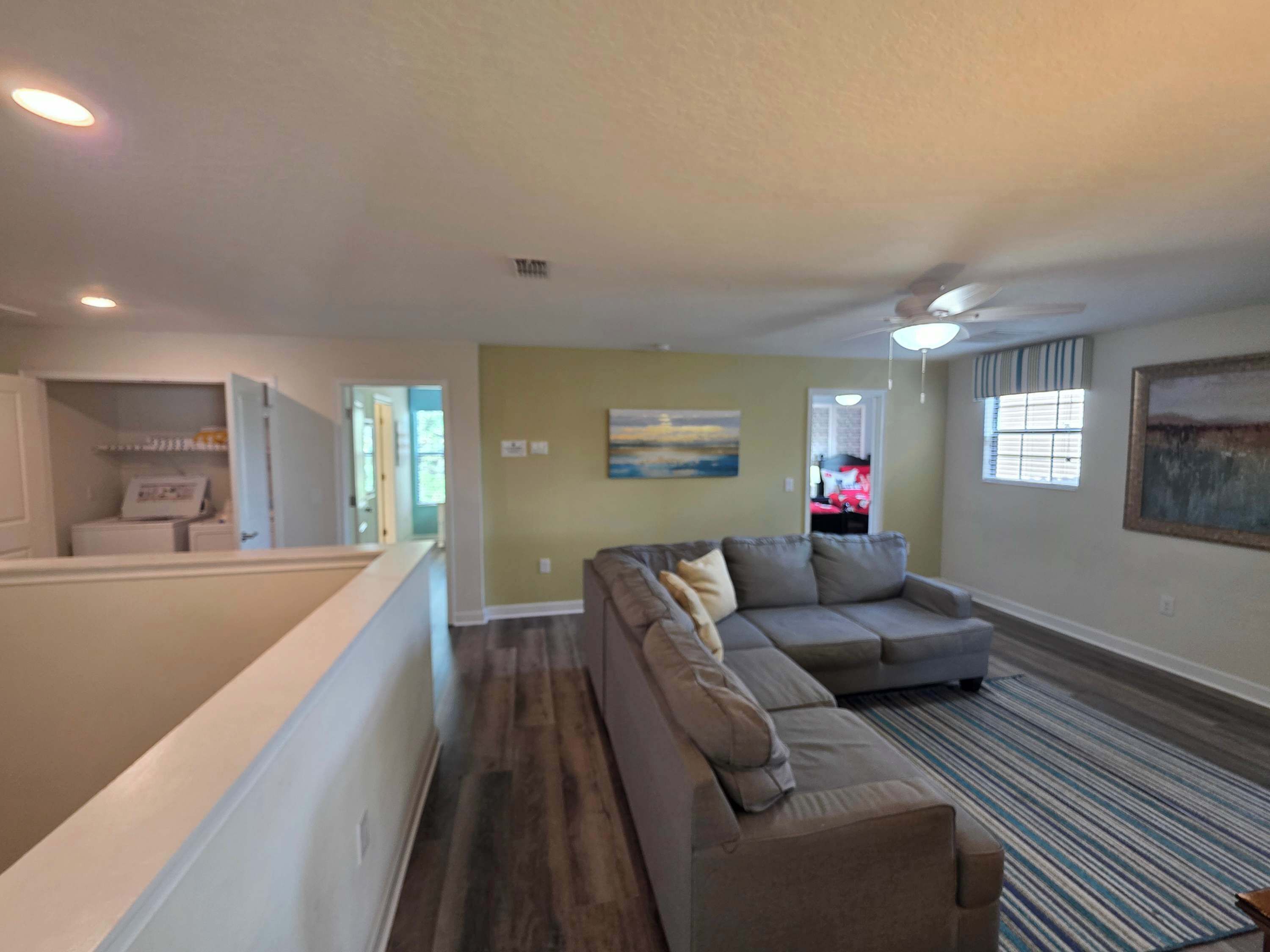 A spacious living room with a sectional sofa, a flat-screen TV, and a large window.