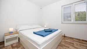 A neatly made bed with white linens, a blue towel, and a bedside lamp on a wooden nightstand. - Pet friendly apartment in Imotski with WiFi (Imotski)