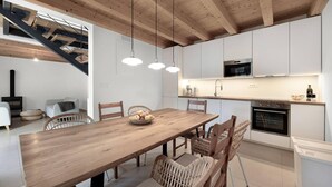 A modern kitchen with white cabinets, a wooden dining table, wicker chairs, pendant lights, and a built-in oven. - Amazing home in Funtana (Funtana)