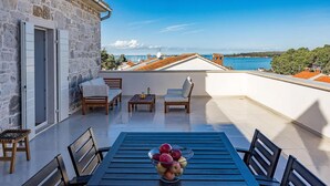 A terrace with a stone wall, wooden furniture, and a table with fruit. - Amazing home in Funtana (Funtana)