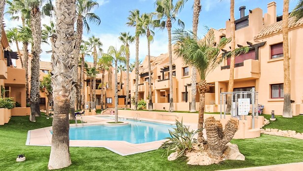 A pool surrounded by palm trees and a building with balconies.