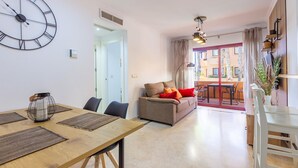 A modern living room with a sofa, a dining table with chairs, and a large wall clock.
