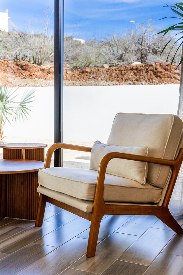 A modern chair with a cushion, a round wooden table, and a view of a desert landscape through a large window.