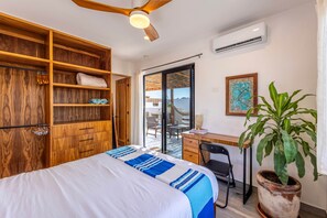 Une chambre comprenant un lit, un bureau, une chaise, une plante en pot et une porte-fenêtre coulissante donnant sur un espace extérieur.