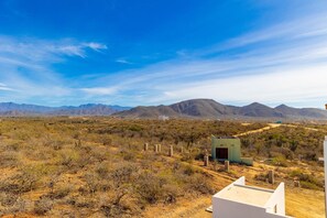 A desert landscape with mountains in the background, sparse vegetation, and a few buildings.