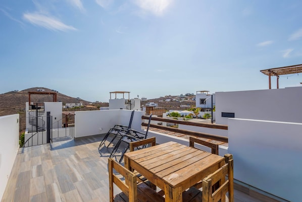 Une terrasse sur le toit, avec une table et des chaises en bois, une pergola et une vue sur le paysage environnant.