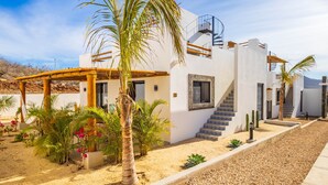 A modern two-story house with a staircase, palm trees, and a sandy garden. - El Corazón Contento | Cerritos Beach (La Paz)