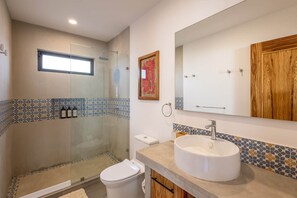 A bathroom with a glass shower enclosure, a toilet, a sink with a mirror, and a decorative tile border.