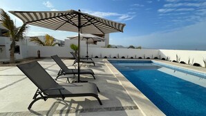 A poolside area with lounge chairs and umbrellas, a clear blue pool, and a view of the ocean. - El Corazón Contento | Cerritos Beach (La Paz)