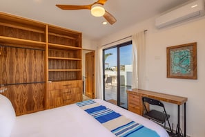 A bedroom with a bed, a desk, a chair, a ceiling fan, a wardrobe, and a sliding glass door leading to a balcony. - El Corazón Contento | Cerritos Beach (La Paz)