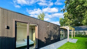 Ein modernes Gebäude mit Glastür, einem sichtbaren Bett im Inneren und einem gepflegten Rasen.