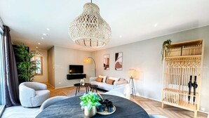 Ein modernes Wohnzimmer mit einem runden Couchtisch aus dunklem Holz, einem grauen Sessel, einem weißen Sofa, einer großen gewebten Pendelleuchte und einer Holzkommode mit Regenschirmen.