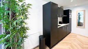 Eine moderne Küche mit dunklen Schränken, einer schwarzen Mülltonne und einer Bambuspflanze.