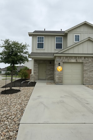 A two-story house with a front garage, a small tree, and a well-maintained driveway.