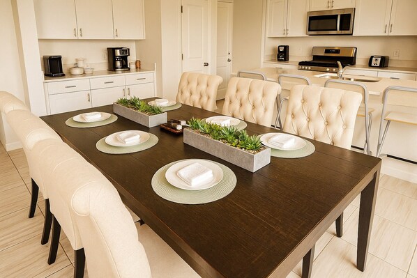 A dining area with a dark wooden table, white upholstered chairs, and a central planter with greenery.
