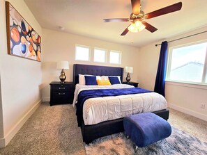A bedroom with a bed, two nightstands, a ceiling fan, and a large window with curtains.