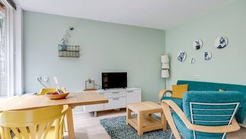 Un salon moderne avec un canapé de couleur turquoise, une table à manger en bois, un téléviseur et des assiettes décoratives accrochées au mur.