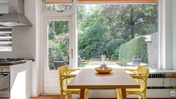 A kitchen with a dining area, a window with a view of a garden, and a table with chairs.