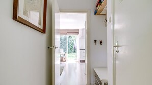 Een gang die leidt naar een kamer met uitzicht op een tuin, een deur met een greep en een plank met boeken.