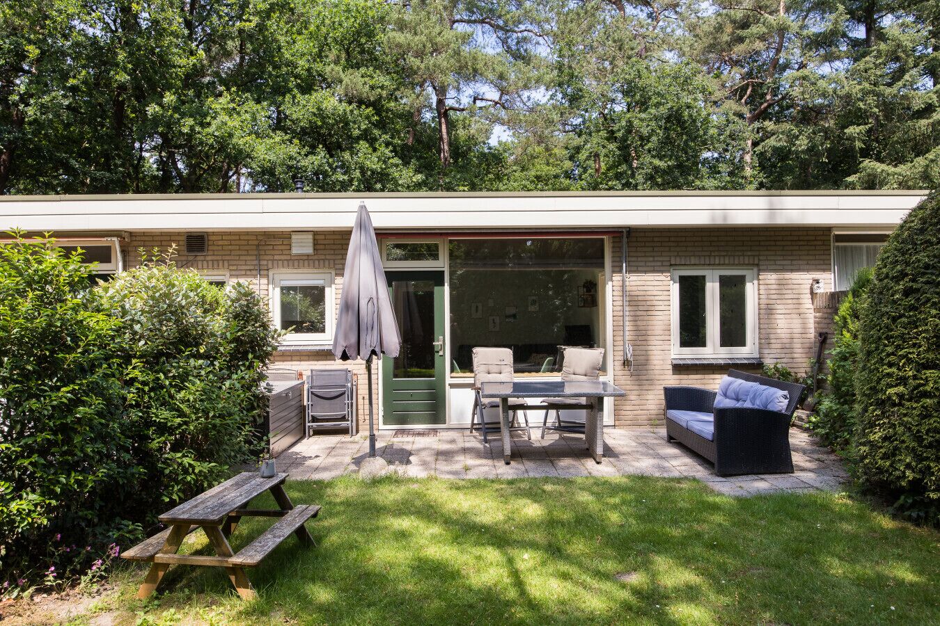 Een huis met een patio, compleet met een tafel, stoelen en een parasol. Er is een groene deur en een raam met uitzicht op het interieur.