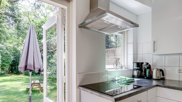 Een moderne keuken met een groot raam, een ingebouwde kookplaat en een fiets die tegen het raam leunt.