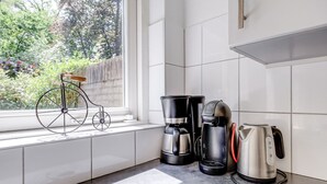 Een keuken met witte tegels, een raam met uitzicht op groen, een fiets en koffiezetapparaten.