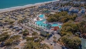 Oversigtsbillede af en kystferieort med en stor swimmingpool, campingvognsparkering og ejendomme ved stranden.