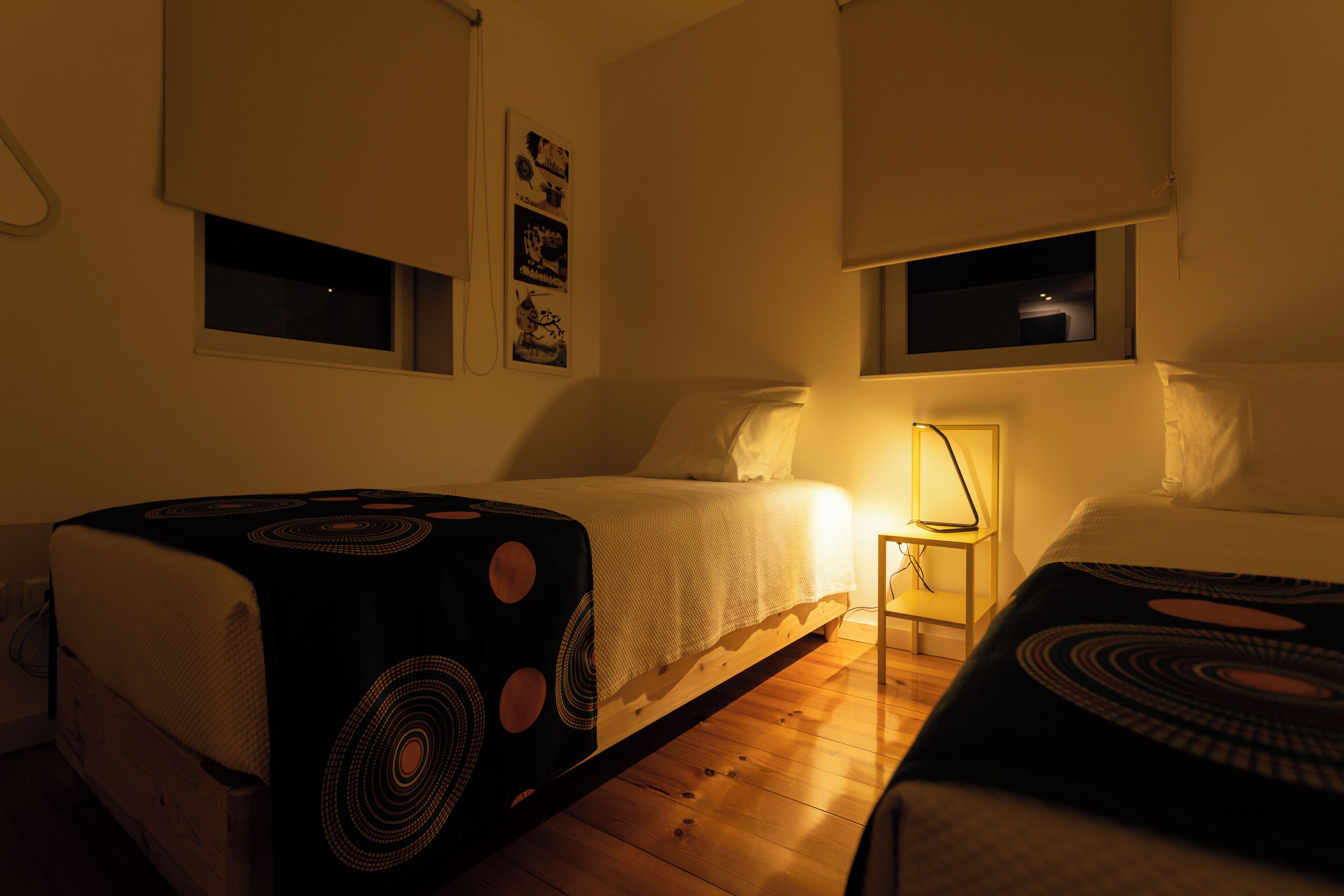A bedroom with two beds, a nightstand, and a wall-mounted lamp.