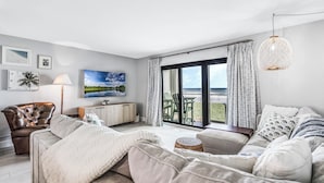 Una sala de estar moderna con un sofá, una silla, un televisor y vistas al exterior.