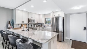 Una cocina moderna con armarios blancos, electrodomésticos de acero inoxidable y una isla de mármol con taburetes de bar.