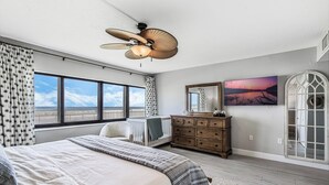 Un dormitorio con una cama grande, ventilador de techo, cómoda, cuna y un ventanal con vistas a la playa.