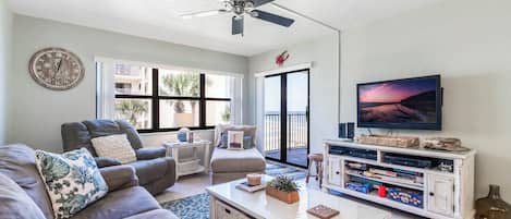 Una sala de estar con sofá, mesa de centro, televisión y un balcón con vistas.