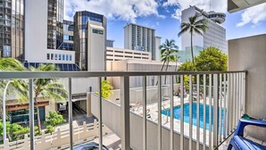 Un balcón con vistas a una piscina, palmeras y edificios modernos al fondo.