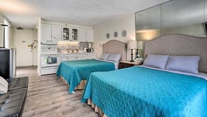 Habitación compacta con dos camas, kitchenette y una pequeña zona de estar.