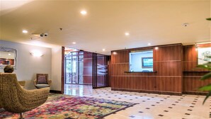 Un vestíbulo de hotel con una recepción, una alfombra colorida y una silla de mimbre.