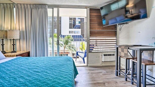 Habitación de hotel con cama, televisión montada en la pared, balcón con una silla y escritorio con silla.