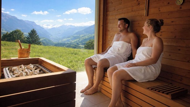 A wooden sauna with a view of mountains, a wooden bench, and a stone basin.