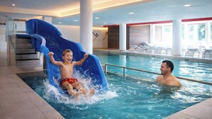 An indoor swimming pool with a blue slide, a staircase, and lounge chairs.