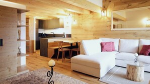 A modern living room with a white sofa, a dining area with wooden furniture, and a kitchen in the background.
