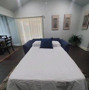 Relax in comfort with a large bed, two chairs, and a small table, surrounded by framed artwork and a potted plant.