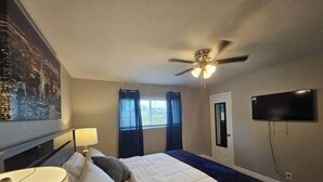 Une chambre d’hôtel avec un lit, un ventilateur de plafond, un téléviseur fixé au mur et une fenêtre avec des rideaux.