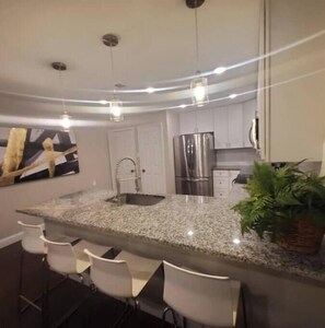 A modern kitchen with a granite countertop, stainless steel appliances, and a bar area with white chairs. - SUPERHOST/Spacious Classy Enclave Rodeo < 1mile. Baby Crib (Mesquite)
