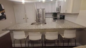 Une cuisine moderne avec des meubles blancs, un îlot central doté de tabourets et un four à micro-ondes.