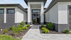 Une maison moderne avec une entrée centrale, deux ailes latérales et un chemin pavé menant à la porte.