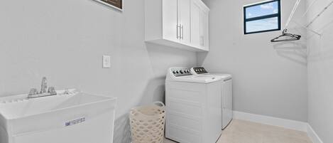 A laundry room with a sink, a washing machine, and a drying rack.
