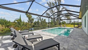Une piscine extérieure couverte, dotée de chaises longues, d’une table et offrant une vue sur un étang et des arbres.