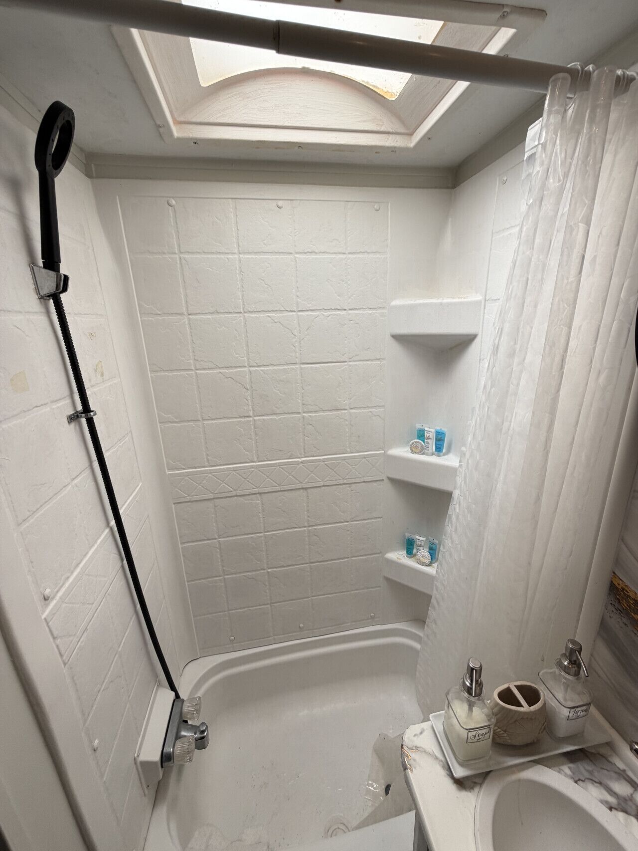 Ein kleines, weißes Badezimmer mit Dachfenster, einer Dusche und einer Toilette.